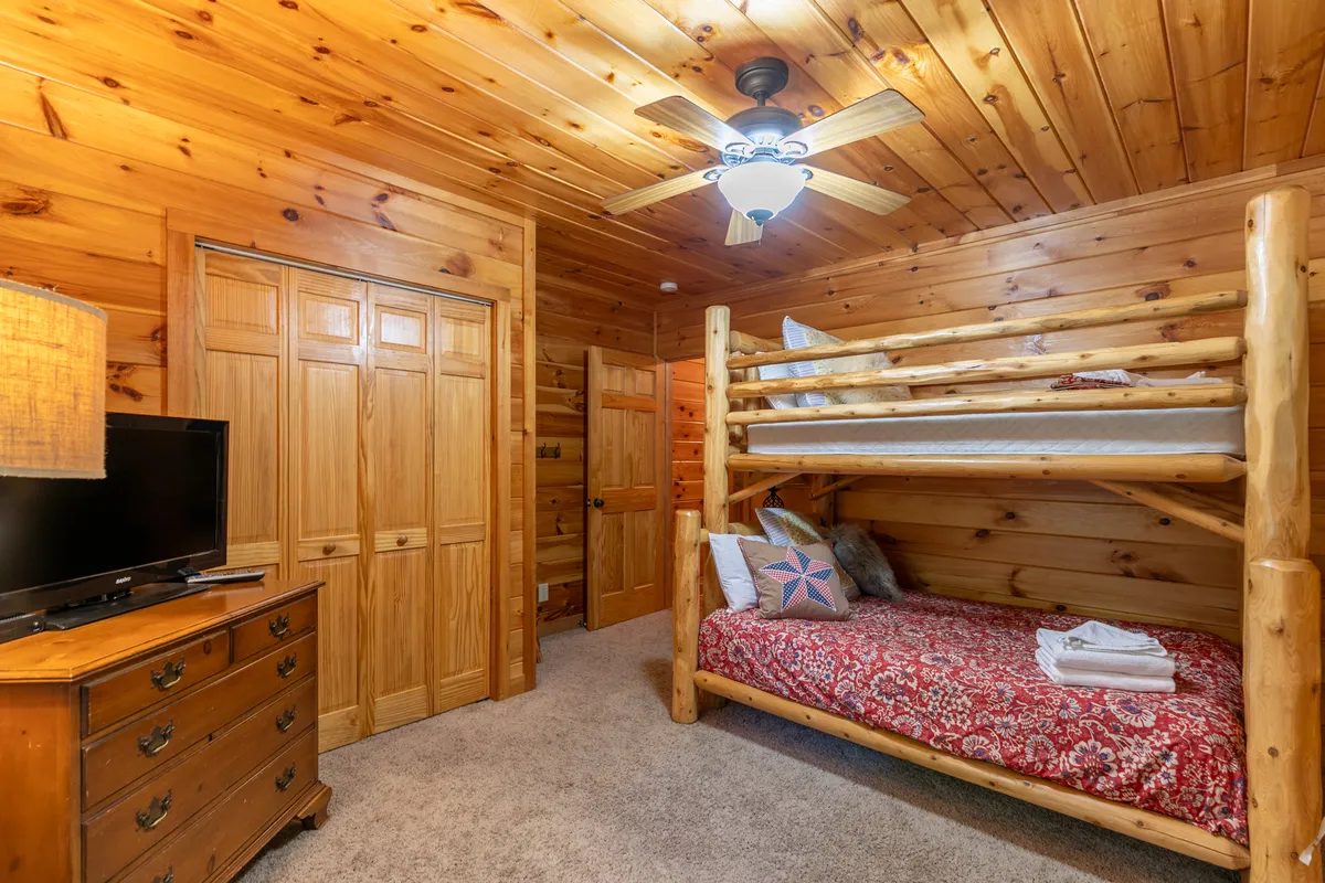 A cozy bunk room with a bunk bed, dresser, TV, and a lamp, blending comfort and entertainment. The room feels intimate and thoughtfully organized, suitable for both children and adults seeking a private sleeping space.
