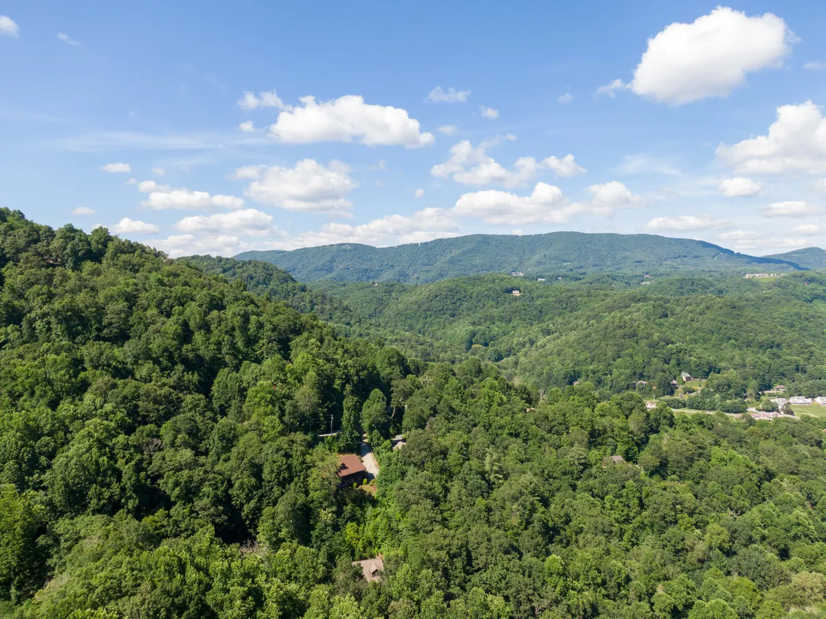 A sweeping view of rolling hills, dense forests, and scattered homes, capturing the expansive mountain scenery and a sense of freedom for outdoor activities like hiking and nature walks.
