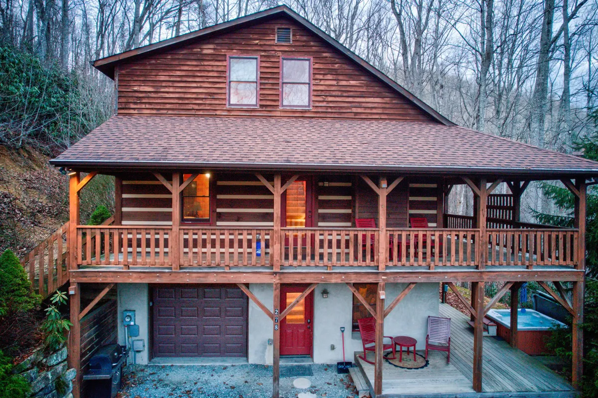 This image shows the front porch of the cabin, featuring a welcoming wooden structure with a hot tub, a red door, and lush trees surrounding the area. The porch offers space for relaxation and socializing, with the calming influence of the natural mountain environment all around.