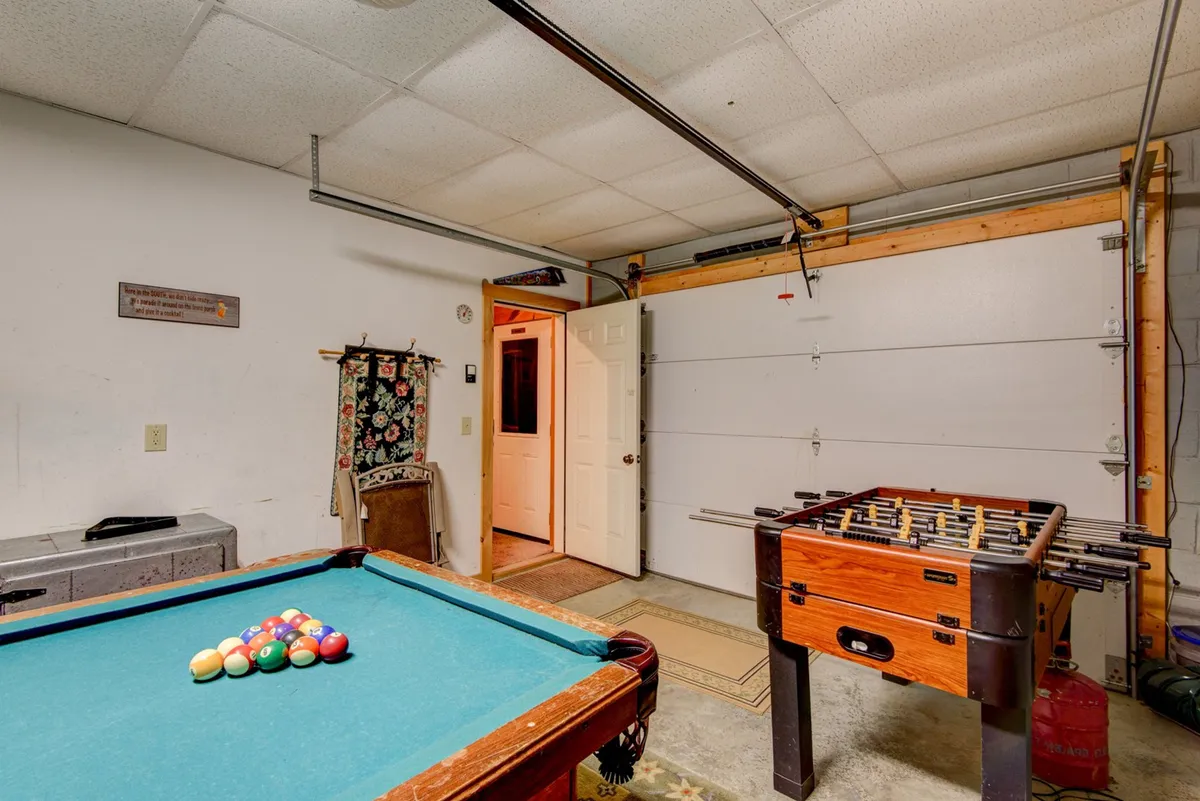 A spacious game room featuring a pool table and foosball table, with a doorway that opens to the outdoors. The room exudes a social and relaxed vibe, ideal for friendly competition among friends.