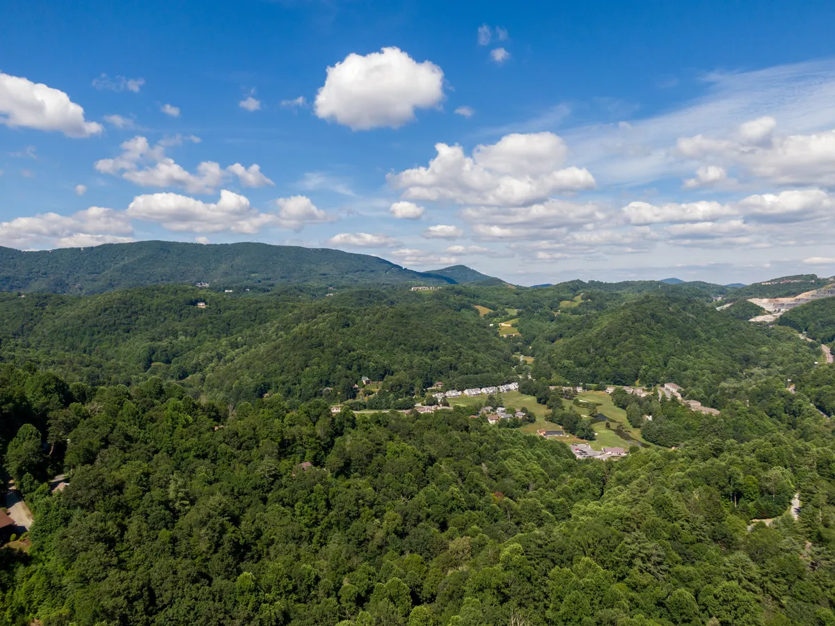 An expansive view of rolling green hills and distant mountains, with scattered clouds overhead. The untouched landscape invites exploration, suggesting opportunities for hiking, wildlife watching, and photography. The peaceful scene embodies the natural beauty of the Blue Ridge area.