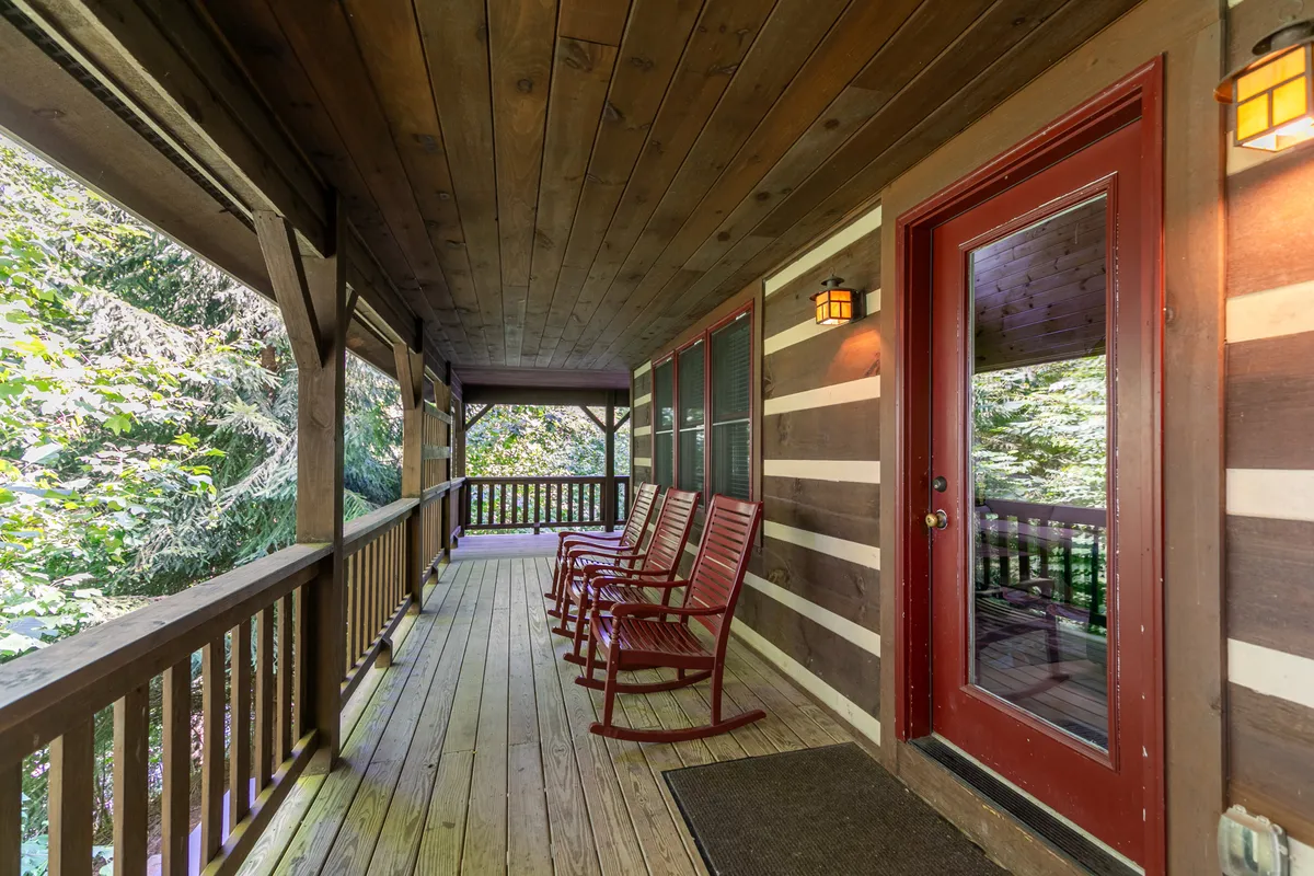 A cozy porch scene with inviting rocking chairs, wooden beams, and views of the surrounding trees. The setup encourages morning coffee, reading, or watching pets play in the yard while soaking up fresh mountain air.