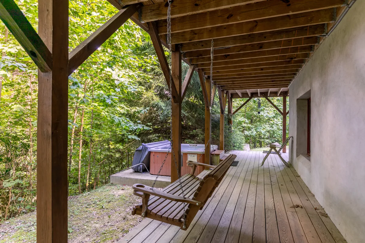 An exterior shot featuring a wooden swing and hot tub nestled amidst lush greenery. The view is peaceful, with the swing offering a spot to enjoy sunset views or quiet reflection. The setting is inviting for both relaxation and socializing in a natural environment.